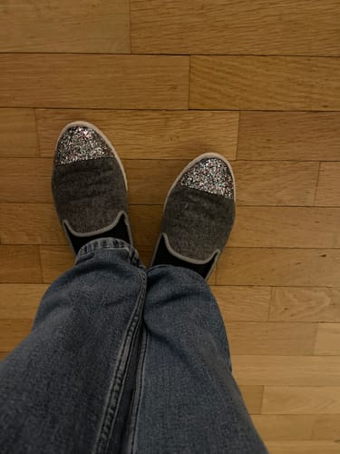 Cliente portant les chaussons Bruson gris à bout pailleté sur un sol en bois.