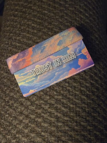 Reviewer's Trust In Him bracelet and card with a colorful cloudscape design, resting on a textured surface.