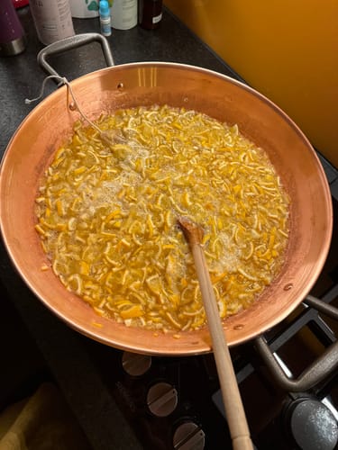 Kunde kocht geschnittene Meyer-Zitronen in einem großen, kupferfarbenen Topf auf dem Herd.