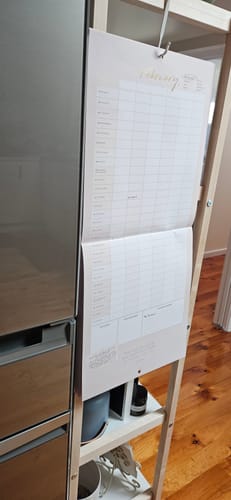 Customer's Blush + Beige Wall Planner open to February, hanging on a wooden shelving unit in their home.