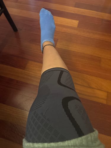 Customer wearing the grey, patterned Premium Bamboo Knee Sleeve on their leg against a wooden floor.