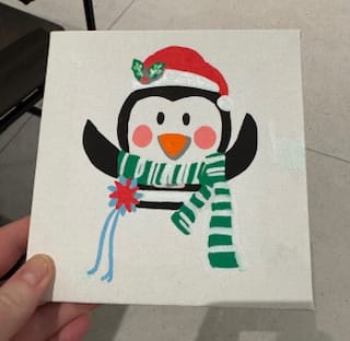Customer holding a completed mini painting of a festive penguin from the Paint by Number Christmas set.