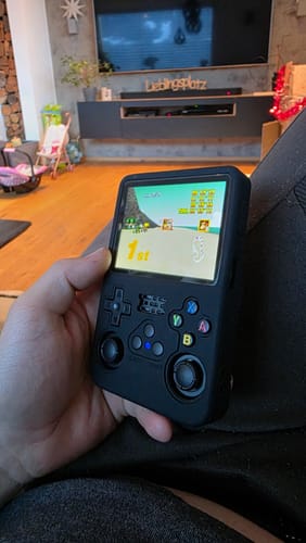 Customer playing a racing game on a handheld console fitted with the black Play Armor protective case.