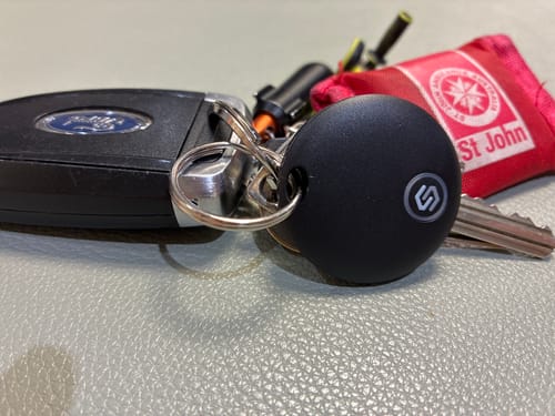 Customer's black SmartTag attached to a keychain with a Ford car key and a red pouch on a textured surface.