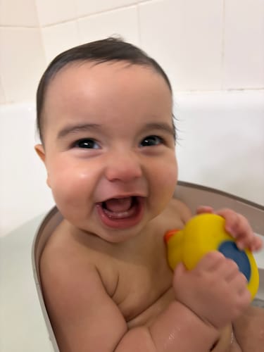 Customer's happy baby smiling in the tub, enjoying bath time with The Wash and Lotion Bundle.