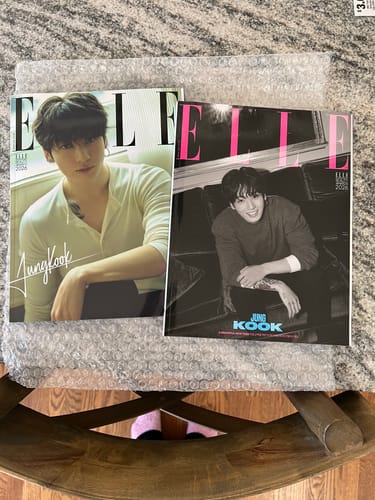 Reviewer shows two different ELLE magazine covers featuring Jung Kook, laid out on bubble wrap packaging.