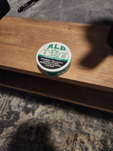 Reviewer's tin of ALP Tropical Fruit nicotine pouches sitting on a wooden surface.