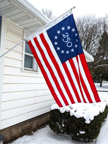 Customer's special '250' anniversary American flag flying outside their home in the snow.
