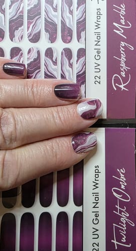 Hand einer Kundin, die eine Maniküre mit den dunklen Twilight Ombré und den marmorierten Raspberry Marble UV-Gelfolien zeigt.