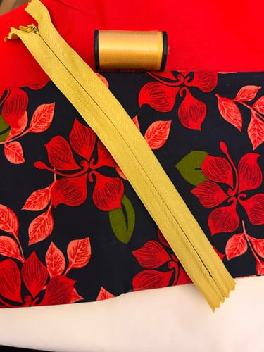 Reviewer's red cotton fabric with a piece of floral fabric, a yellow zipper, and a spool of thread for a project.
