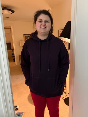 Reviewer standing indoors while wearing the Callie Hoodie in Deep Plum with her hands in the kangaroo pocket.