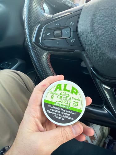 Customer's hand holding a can of ALP Spearmint Nicotine Pouches inside a car.