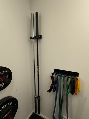 Kunde zeigt seine schwarze Delta-Langhantel, die vertikal in einer Wandhalterung in einem Home-Gym aufbewahrt wird.