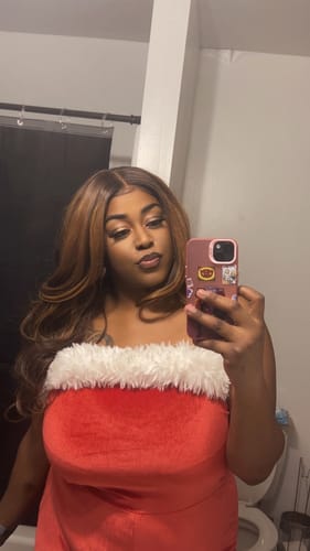 Reviewer in a bathroom taking a mirror selfie wearing the long, wavy Mane Concept Brown Sugar Skinbond Lace Glueless Wig.