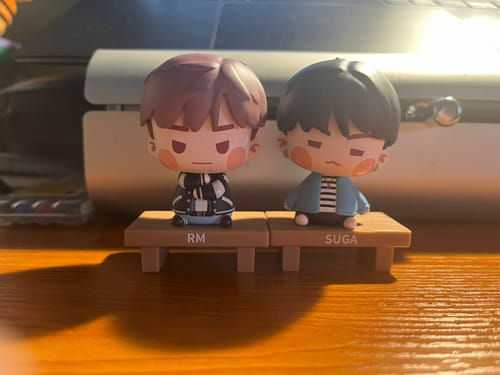 Customer's BTS ISLAND FIGUREs of RM and SUGA sitting on their benches. The two cute figures are displayed on a wooden desk.
