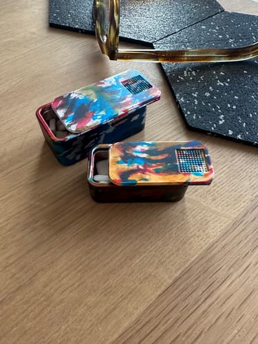 Customer's two Secret Menu pill cases with a vibrant multi-colored design on a wooden surface, one open.
