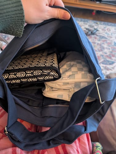 A reviewer holds open their navy blue ALTA bag, showing the spacious interior filled with personal items and multiple zippered compartments.