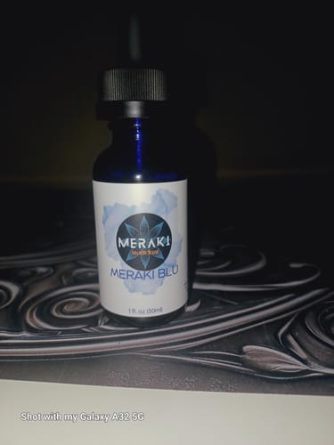 A reviewer's blue bottle of Meraki Blu Methylene Blue sitting on a patterned surface in a dark room.