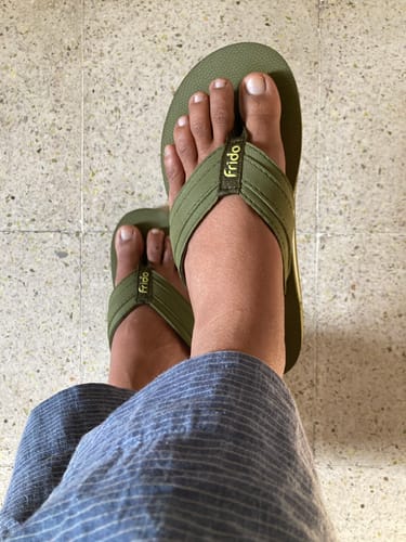 A customer's feet wearing a pair of olive green Frido flip-flops with yellow branding on the straps.