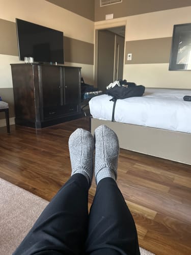 Reviewer relaxing with feet up, wearing gentle grey Gripper Slippers in a hotel room.
