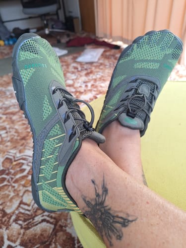 Customer relaxing with feet crossed, wearing the green and grey Free Ⅰ - Barefoot Shoes.