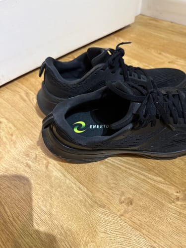Customer's Enertor running insoles placed inside a pair of black running shoes on a wooden floor.
