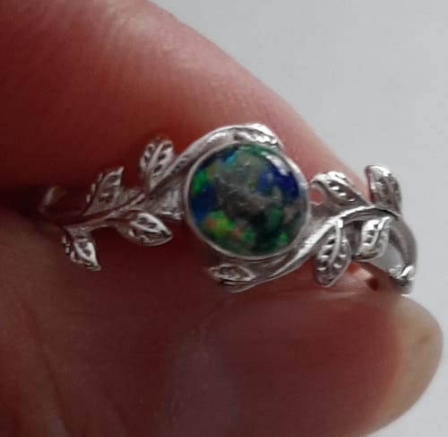 Reviewer's close-up of the Leaf Opal Cremation Ring, showing the silver leaf band and colorful central stone with ashes.