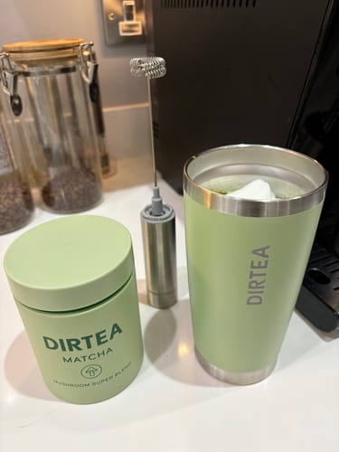 Customer's DIRTEA Matcha container next to a prepared matcha drink in a branded travel mug, with a milk frother nearby.