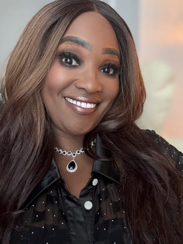 Reviewer smiling while wearing the long, wavy Outre JAANAY wig with reverse ombre color.