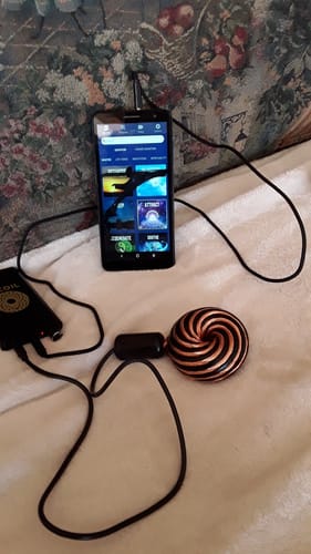 Reviewer's Qi Coil™ Mini System laid out on a white blanket, connected to a smartphone displaying the wellness app.