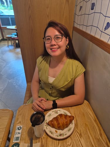 Reviewer smiling at a cafe table while wearing the lightweight Vera Necklace.