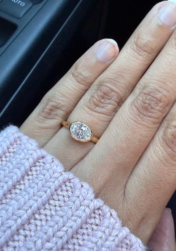 Reviewer's hand wearing The Milgrain oval ring with a gold bezel setting against a pink sweater.