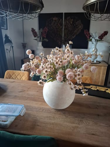 Klant toont de ronde, beige Terra vaas gevuld met bloemen op een houten eettafel.