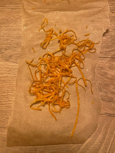 Nahaufnahme von getrockneten, orangen Zesten aus der Bio Orangen-Mixbox auf einem Stück Papier.