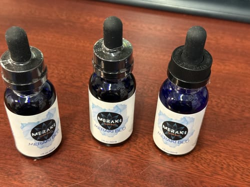 Customer's three bottles of Meraki Blu Methylene Blue with droppers arranged on a wooden desk.