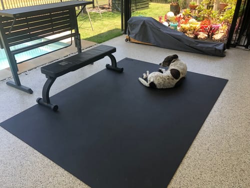 Customer's large Miramat Giga exercise mat set up on an outdoor patio with a workout bench and a dog resting on it.