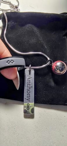 Reviewer's hand places the dark gray silicone wedding ring onto a necklace as a tribute.