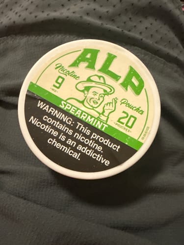 Reviewer's can of Spearmint Nicotine Pouches with its green and white label, shown on a gray textured fabric.