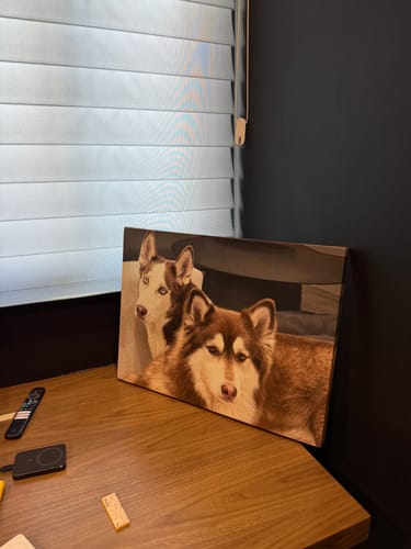 Cuadro canvas de un cliente con la foto de dos perros, apoyado sobre un escritorio de madera.