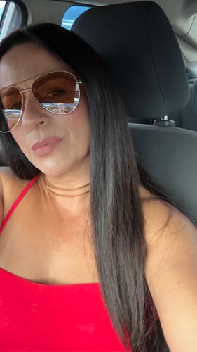 Cliente usando o óculos Savona com lentes laranjas e armação dourada dentro de um carro.