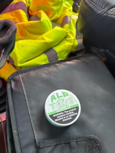 Customer's can of Peppermint Nicotine Pouches resting on a black bag next to a high-visibility jacket.
