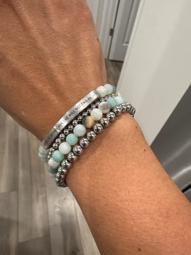 Customer wearing the 'GOD IS WITHIN HER' bundle, showing three stacked bracelets: one engraved, two beaded.