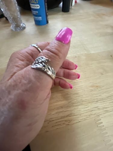 Customer's hand wearing a silver feather-design ring on their thumb against a wooden table background.