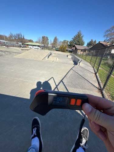 Reviewer holding the black Meepo M6C Remote in their hand at a sunny outdoor skatepark.