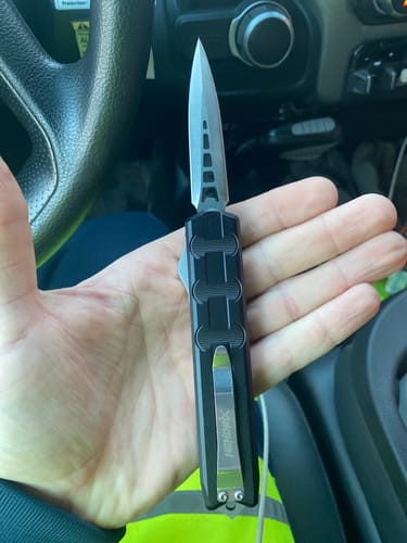 Customer holding their black Hendrix Gear Triton OTF knife with the dagger-style blade extended.