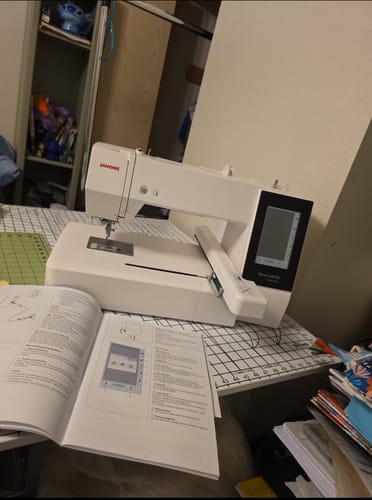 Customer's Janome Memory Craft 500E Embroidery Machine set up on a work table with the instruction manual open in front.