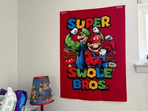 Reviewer's colorful Super Swole Bros Tapestry hanging on a wall in a child's bedroom.