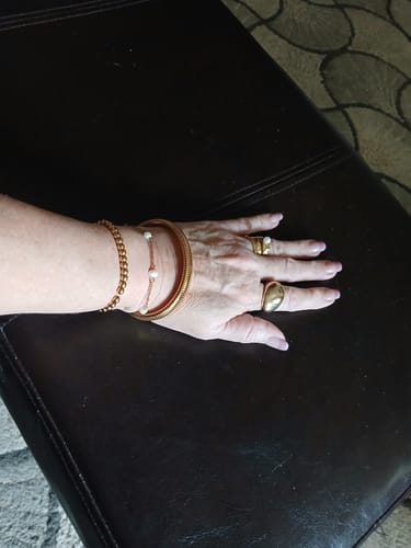 Customer's hand displaying several stacked gold-toned bracelets, one with a rope design, and two rings.