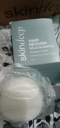 Customer's HAIR REVIVER Solid Shampoo bar in plastic packaging, placed in front of its gray box.