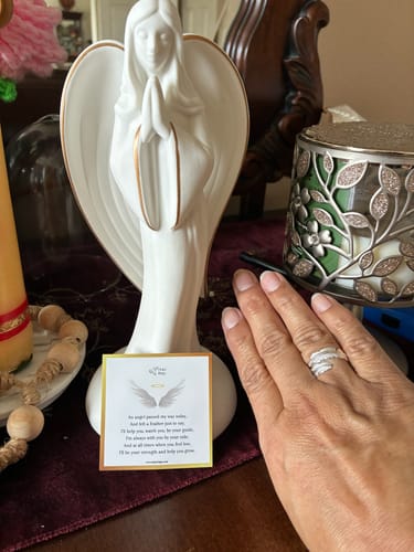 Reviewer's hand wearing the Feather From An Angel Ring next to its message card and an angel figurine.